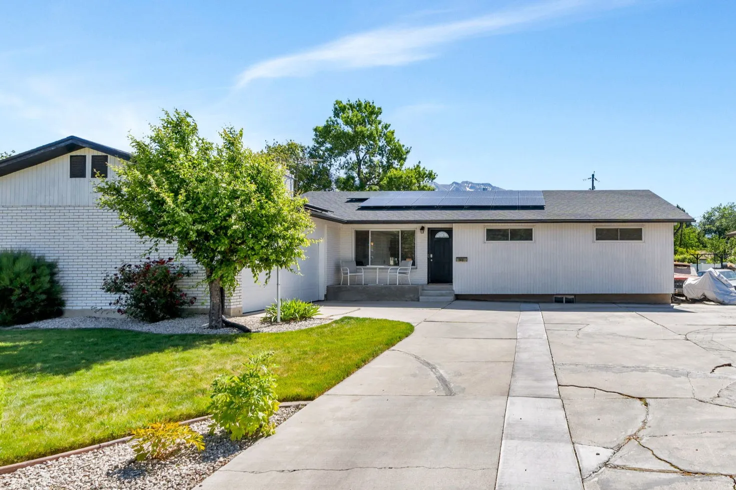 White exterior with a black roof, featuring solar panels and a concrete driveway