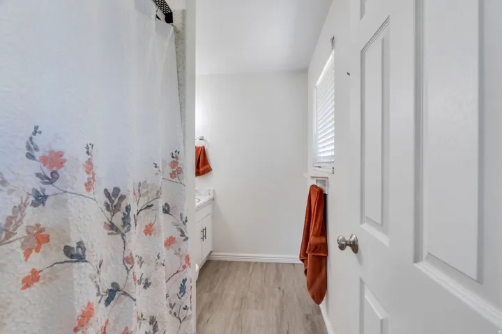 Primary bathroom featuring LVP flooring, a white vanity with a light-colored countertop, a window with blinds and shower