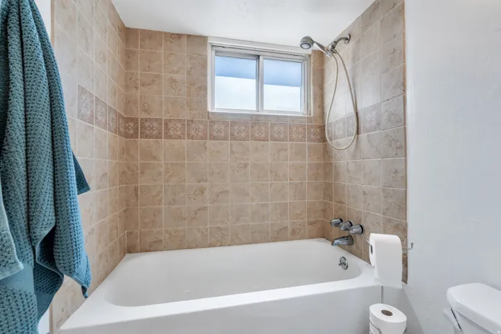 Apartment bathtub and shower combination featuring tiled surround with decorative accent band, chrome fixtures, and an integrated window