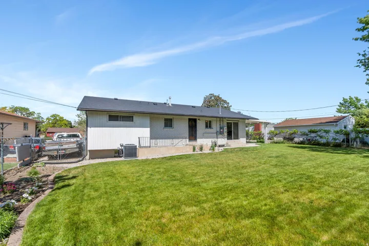 View of rear of the home; Spacious backyard featuring a large grass lawn, a white exterior home with a dark shingle roof, and a concrete patio area