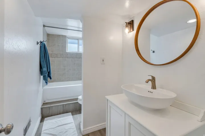 Apartment bathroom featuring a vessel sink with a brushed nickel faucet, a round wood-frame mirror, and a white vanity cabinet