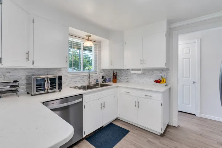 Kitchen featuring white cabinetry, light-toned countertops, stainless steel dishwasher, and wood-finish flooring