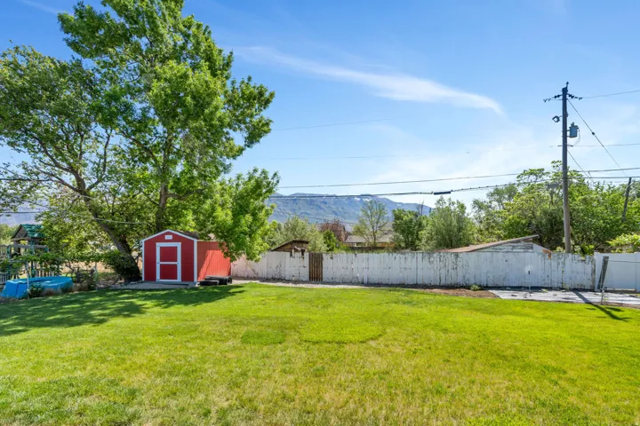 Expansive backyard with a red storage shed, mature trees, and a wooden perimeter fence