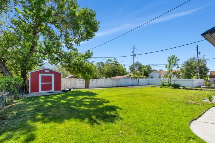 Expansive backyard with a red storage shed, mature trees, and a wooden perimeter fence
