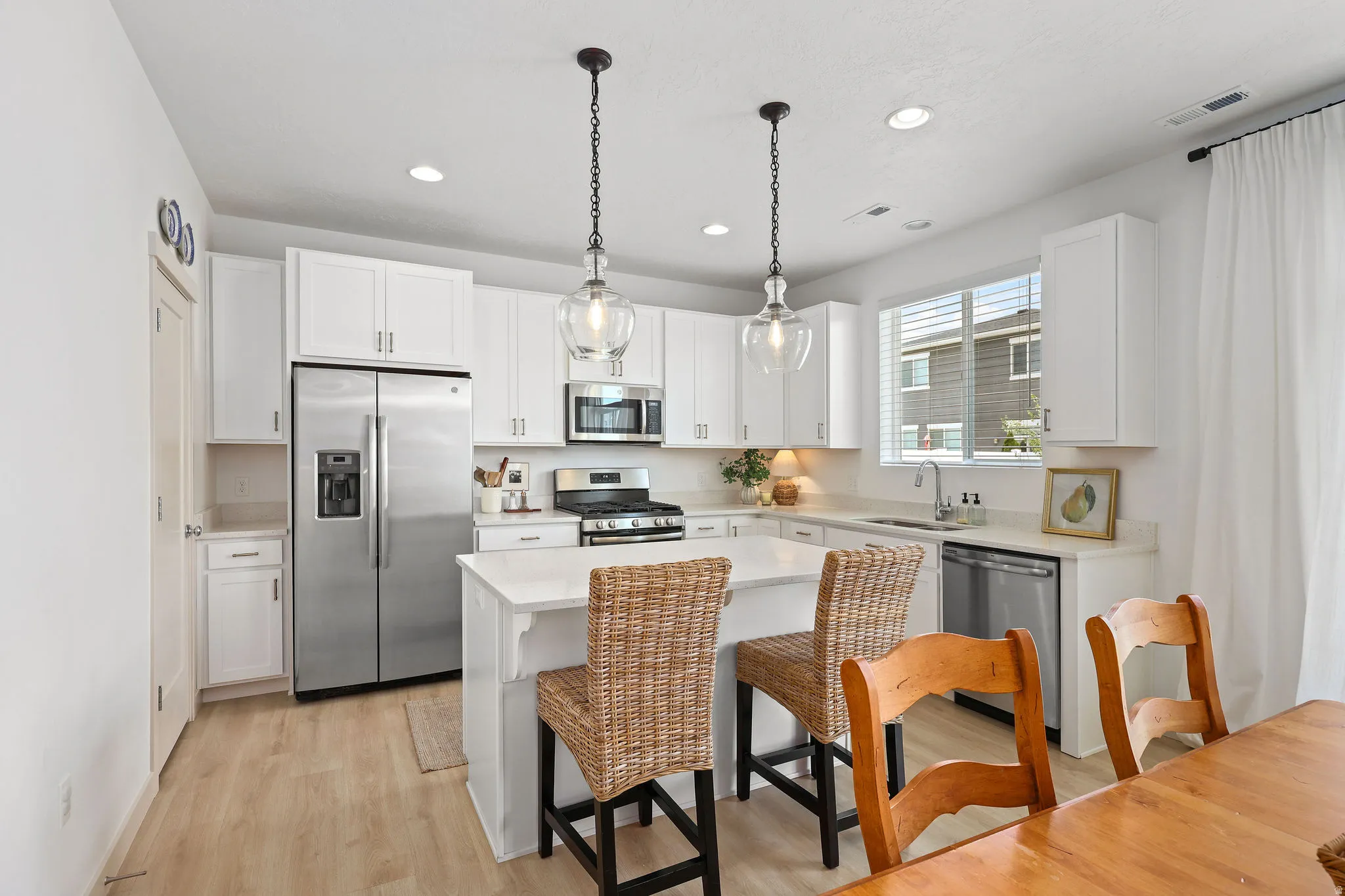 Bright kitchen featuring white cabinetry, stainless steel appliances, a center island with countertop seating, wood-finish flooring, and pendant lighting