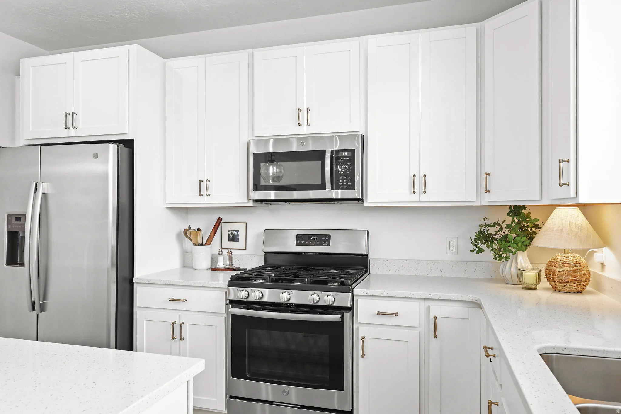 Bright kitchen featuring white shaker-style cabinetry, light-toned countertops, and stainless steel appliances including a refrigerator, range, and microwave
