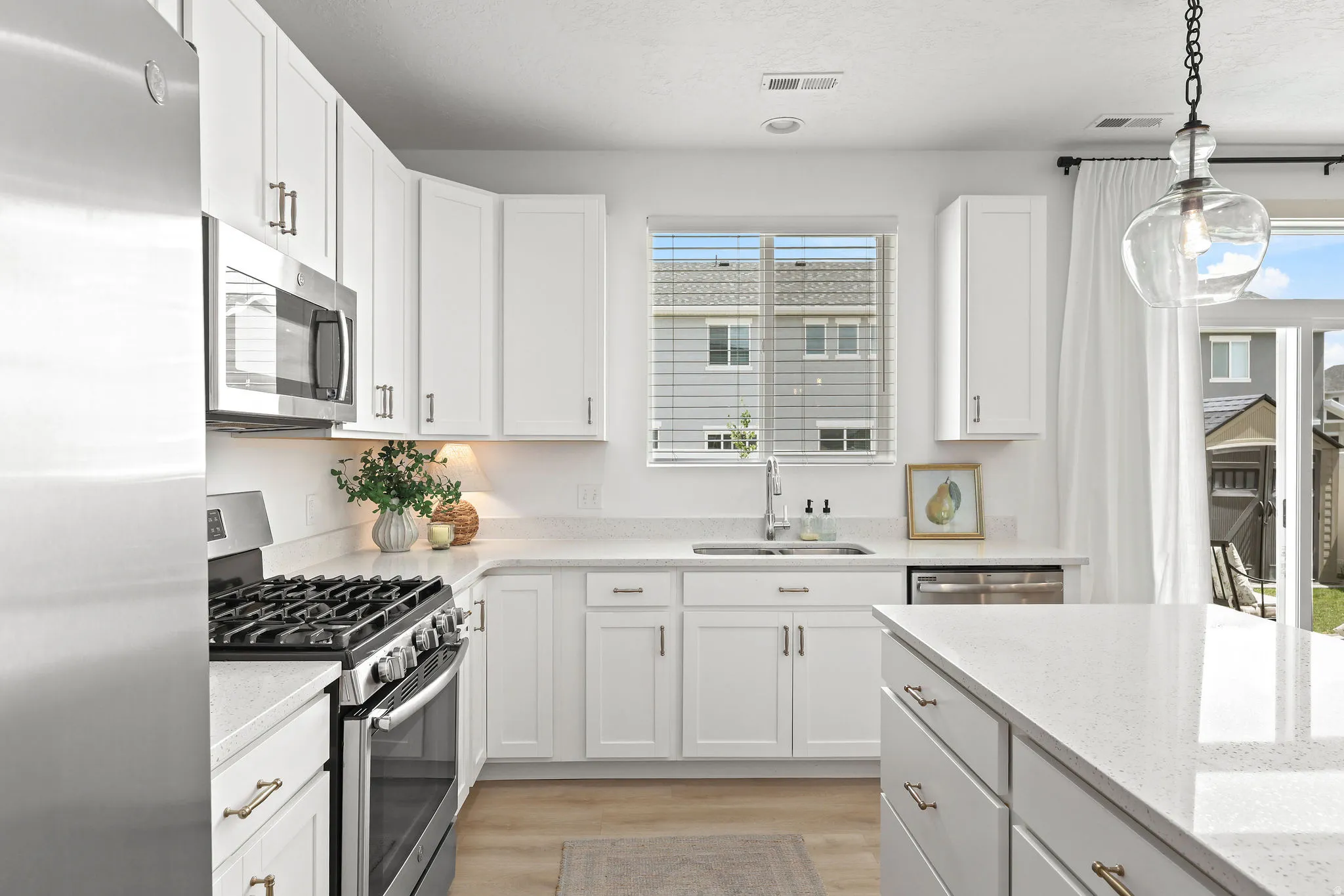 Contemporary kitchen featuring white shaker cabinetry, stainless steel appliances, light-toned countertops, and wood-finish flooring