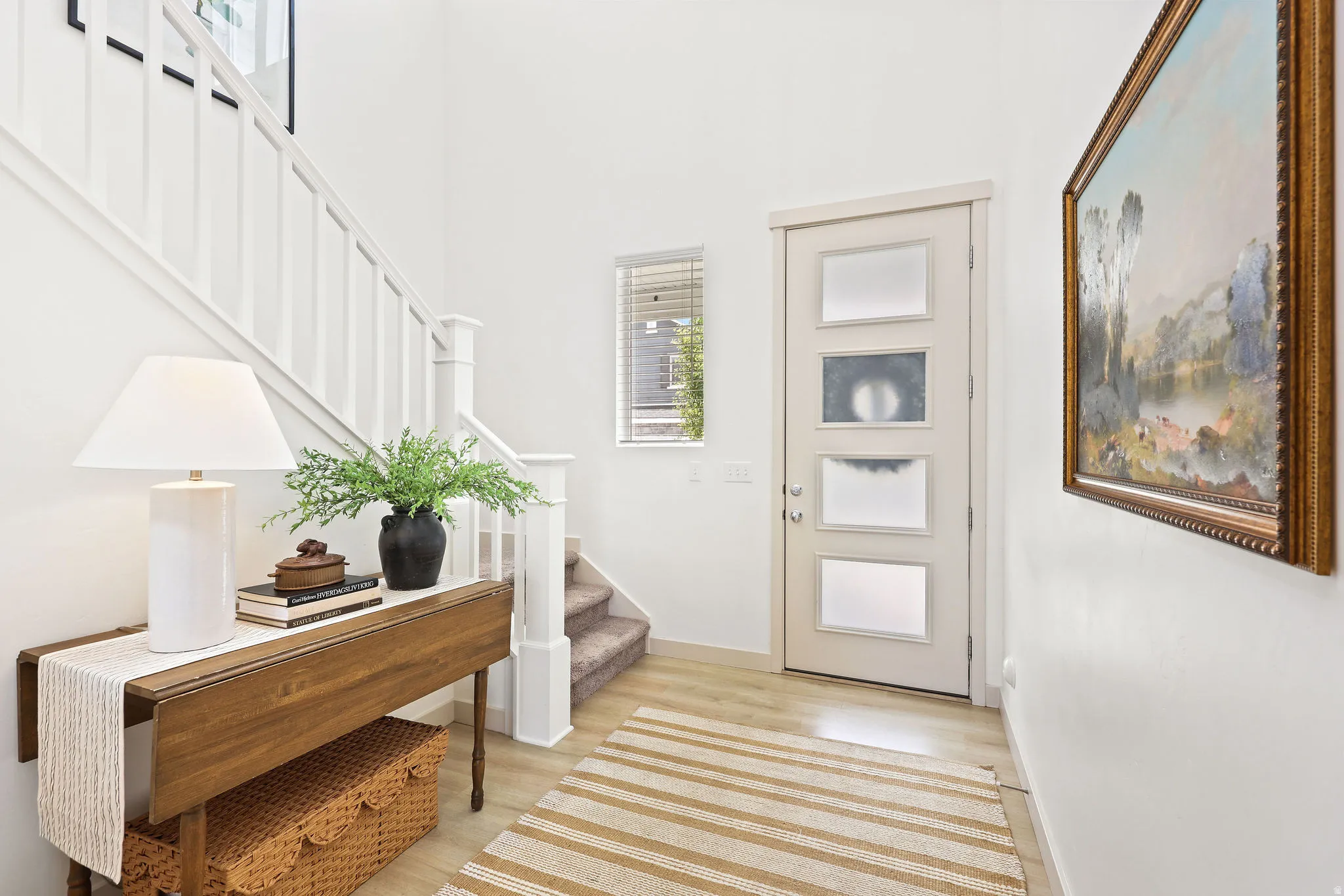 Entryway featuring light wood-finish flooring, a contemporary staircase with white balusters, and a modern door with frosted glass panels