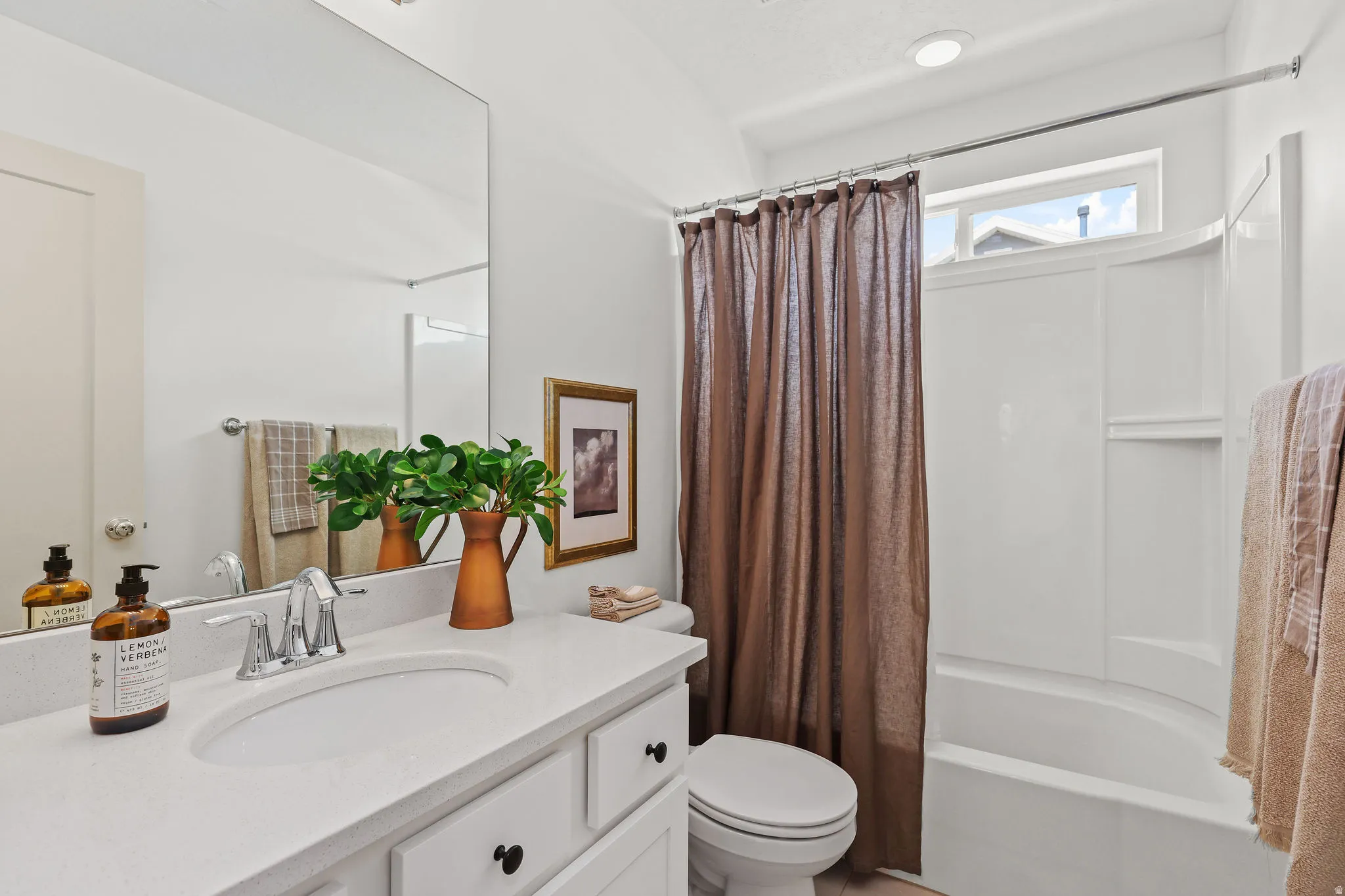 White vanity with a built-in sink and chrome faucet, large rectangular mirror, and an integrated white tub and shower combination with a transom window