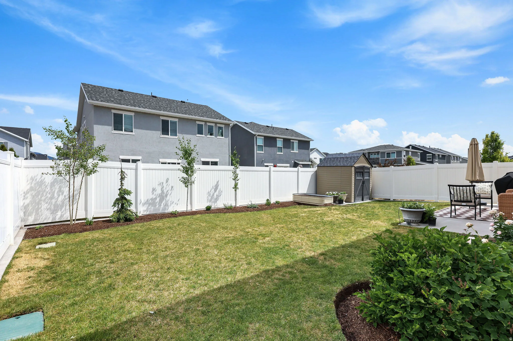 Expansive fenced backyard featuring a manicured lawn, established shrubbery, and a concrete patio area