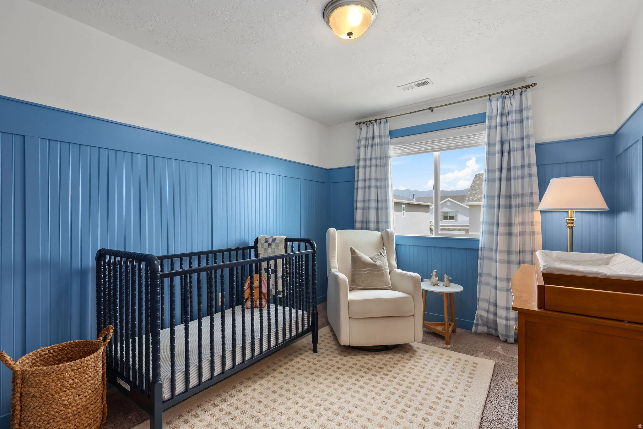 Bedroom featuring blue wainscoting, a large window with white trim, and a patterned area rug