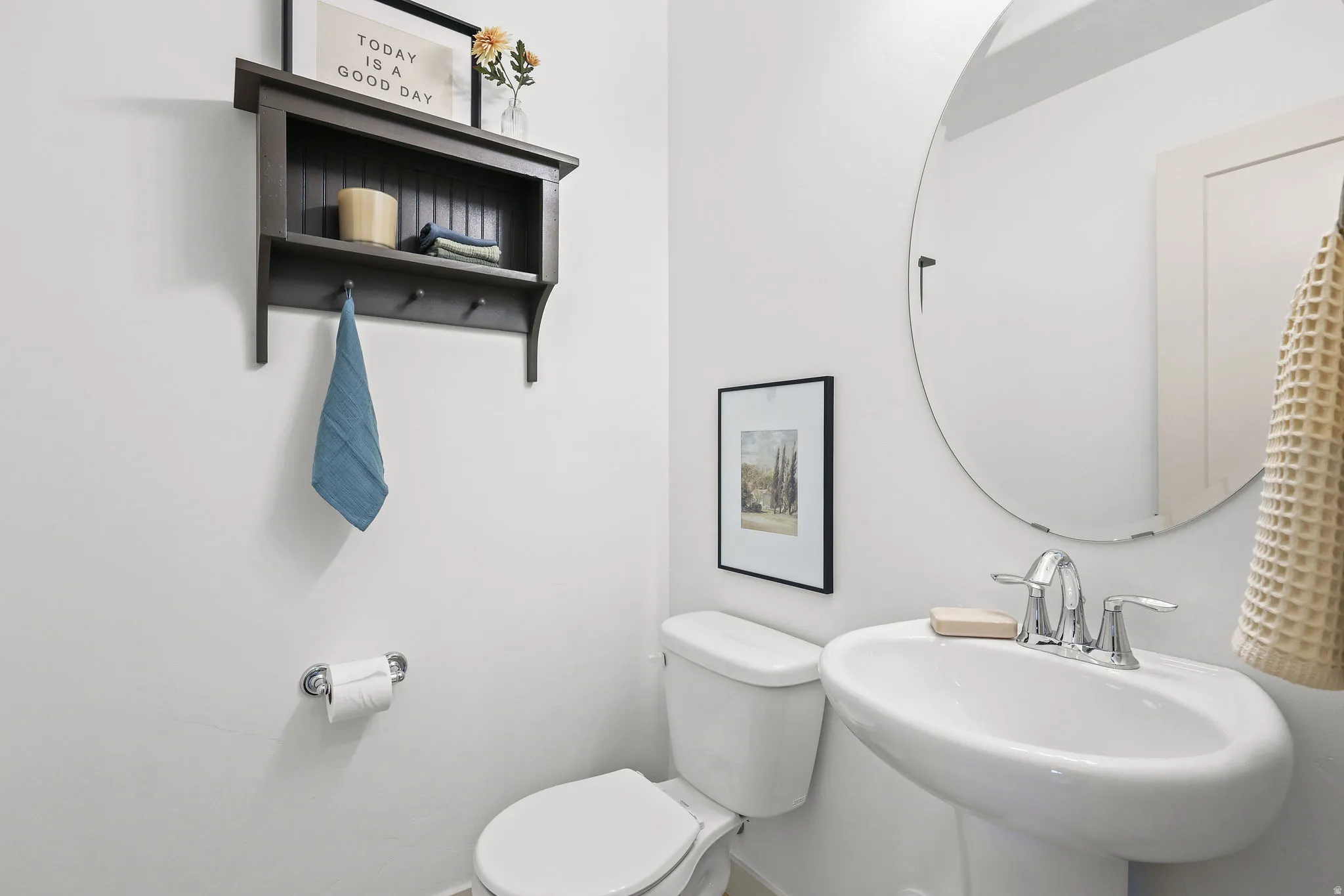 Pedestal sink with chrome fixtures and a circular frameless mirror
