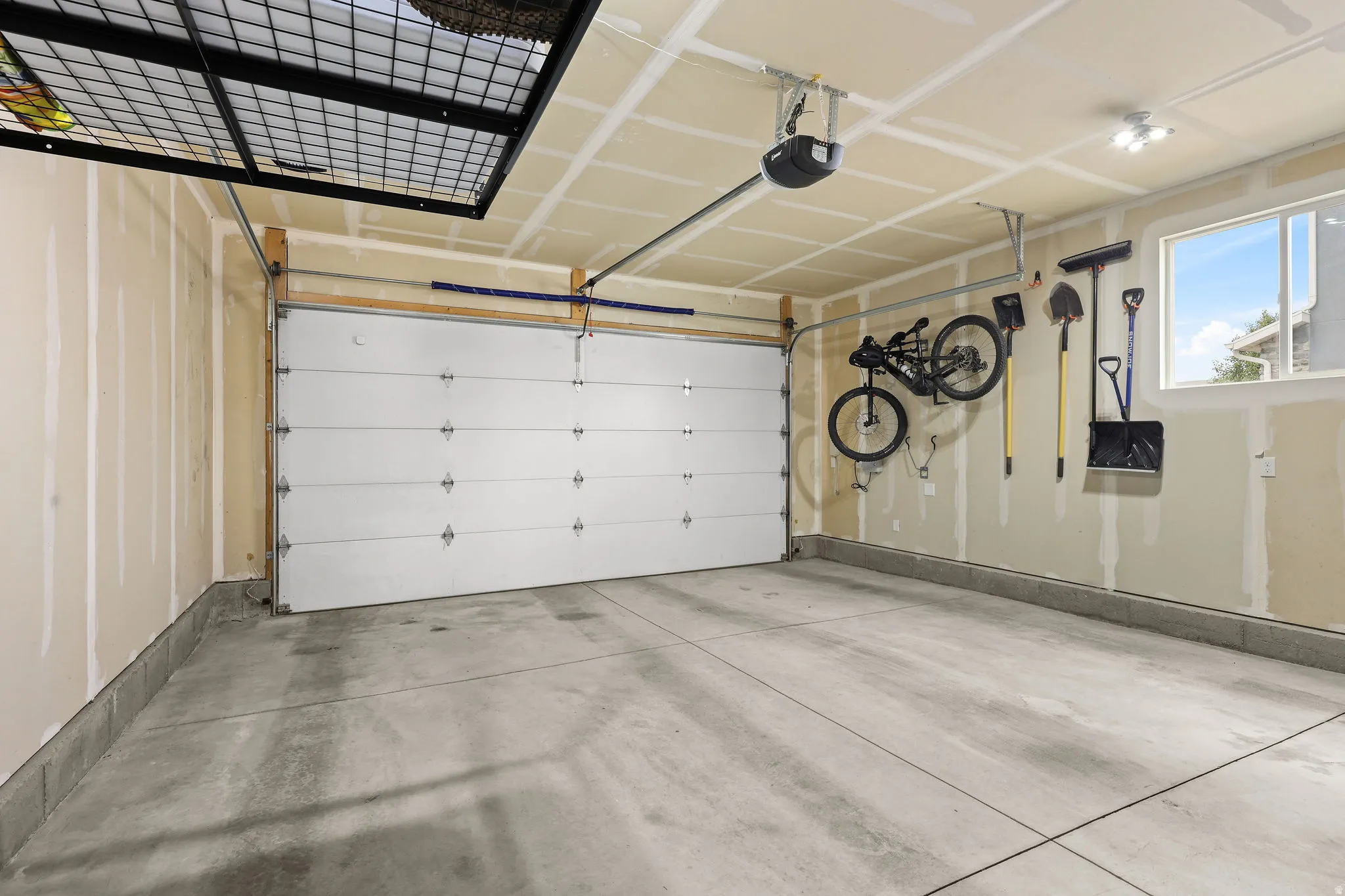Concrete flooring garage with an overhead door, automatic opener, wall-mounted window, and track lighting
