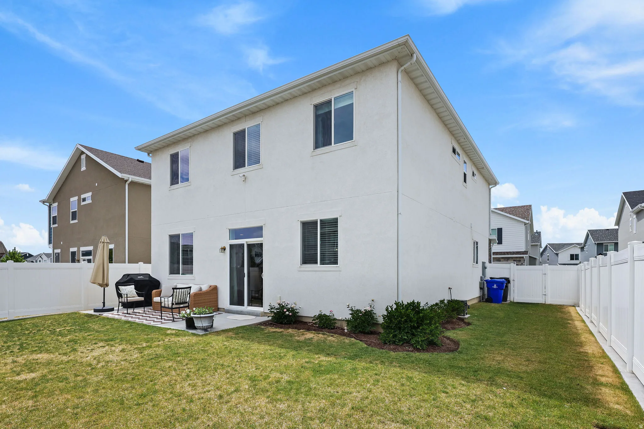 Rear exterior featuring a white stucco facade, multiple windows, a sliding glass door, a concrete patio, and a manicured lawn