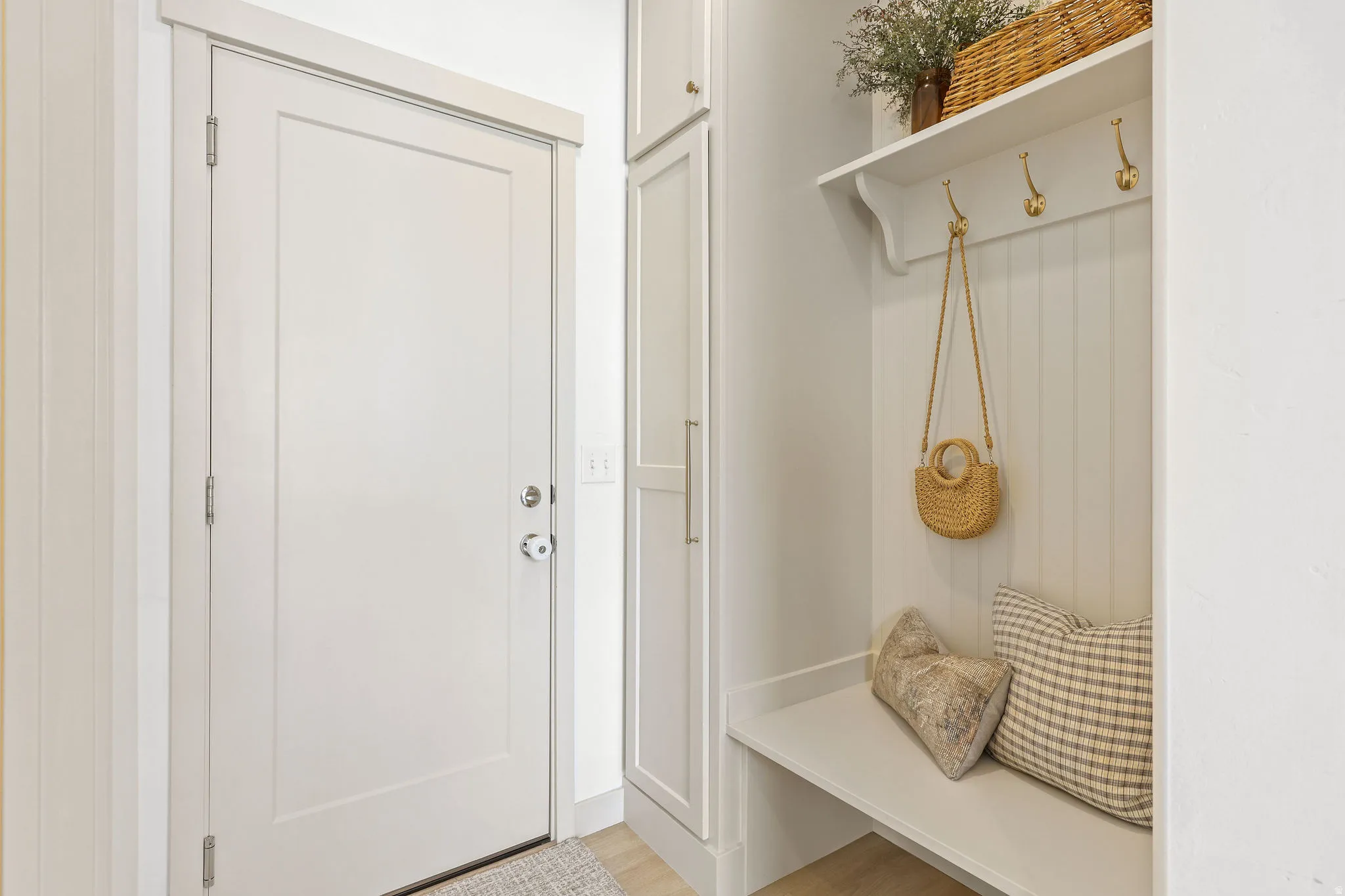 Entryway featuring a white paneled door, built-in storage cabinetry, a bench with beadboard backing, a white shelf, and brass-tone coat hooks