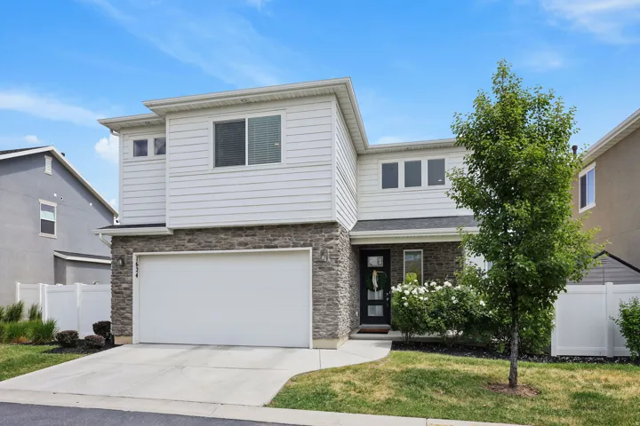 Contemporary facade featuring white horizontal siding, stone veneer accents, an integrated garage, a paved driveway, and mature landscaping