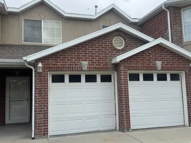 Brick exterior featuring two white garage doors with upper window panels