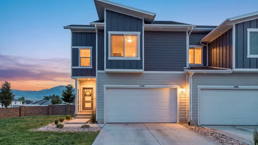 Modern two-story townhome with a two-tone siding exterior, prominent front entry with a full-view door, integrated single-car garage, and a concrete driveway