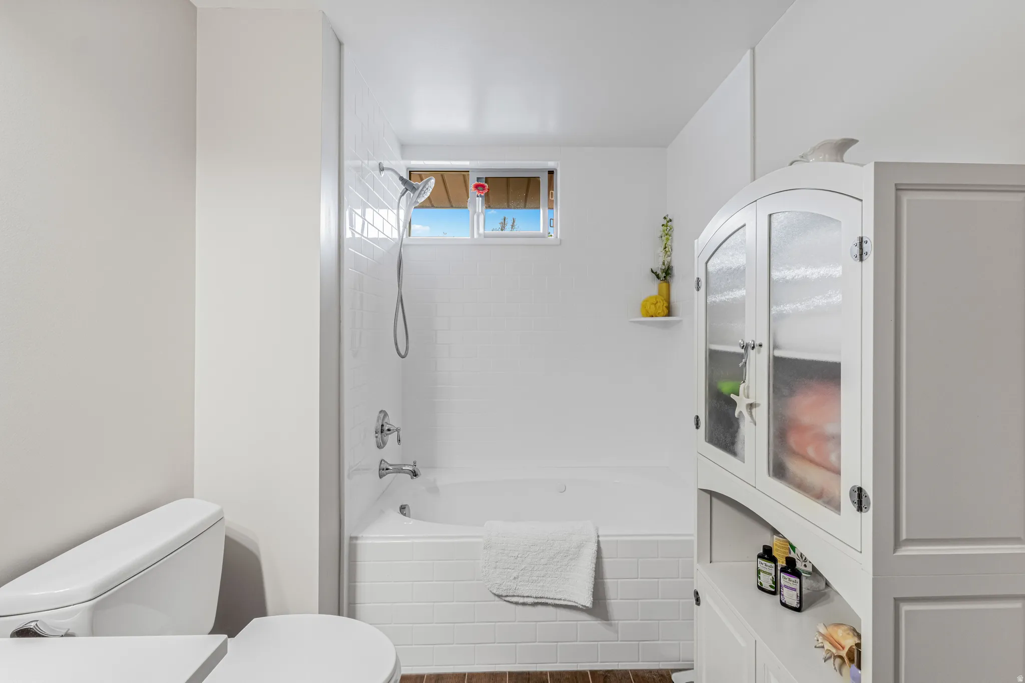 Bathroom featuring a white bathtub, subway tile surround, window, and wood-finish flooring