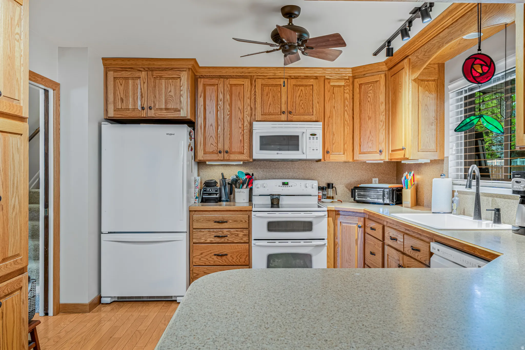 Kitchen featuring wood cabinetry, white appliances including a double oven and microwave, light-colored countertops, and a ceiling fan