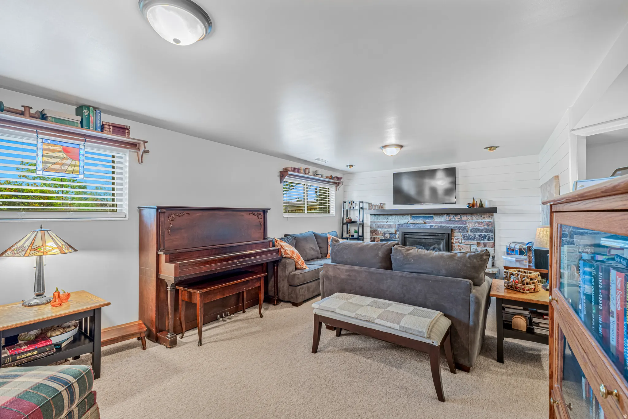Carpeted living space featuring a stone-faced fireplace, shiplap accent wall, built-in shelving, and two windows