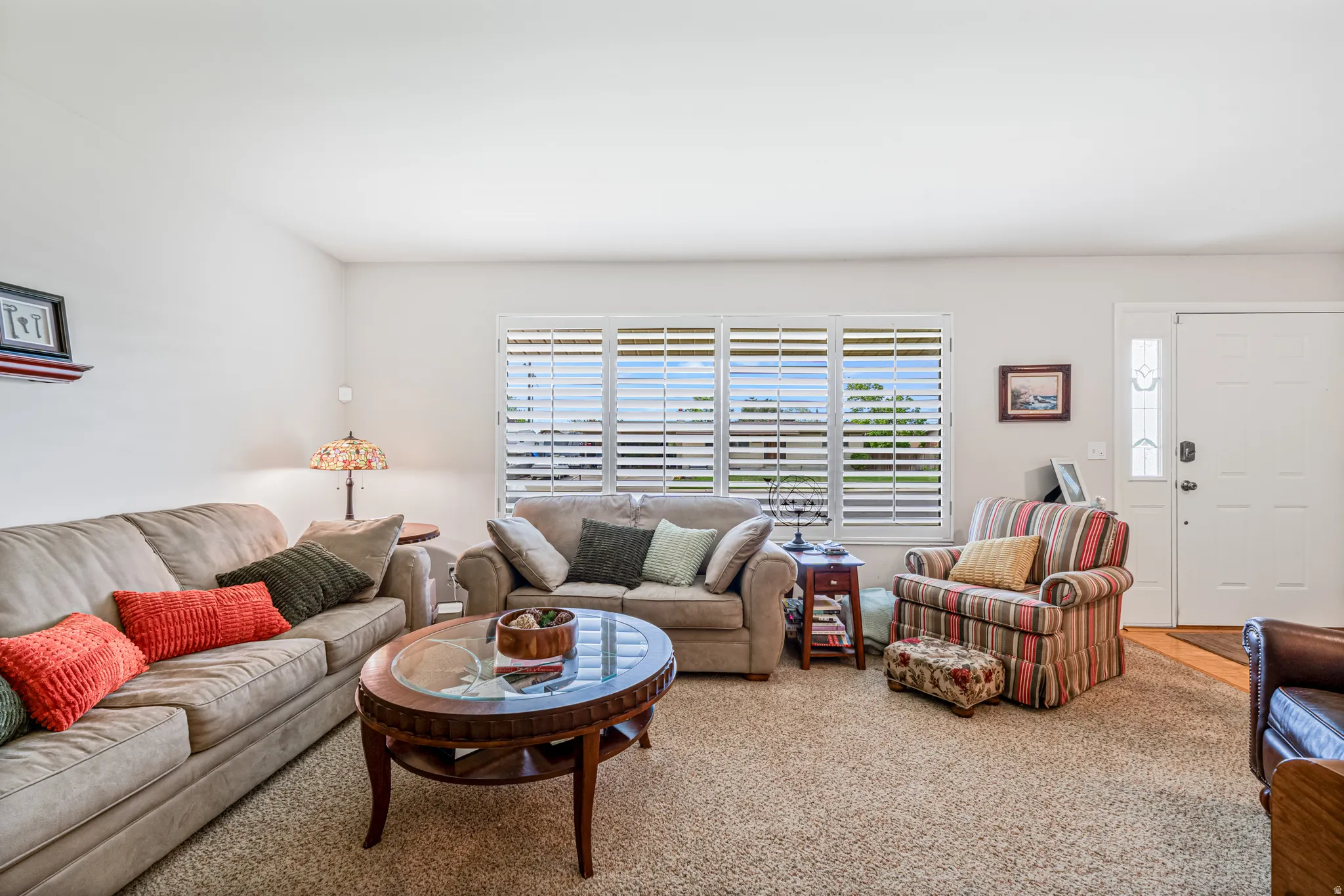 Carpeted living area featuring white walls and a white entry door with a decorative glass sidelight
