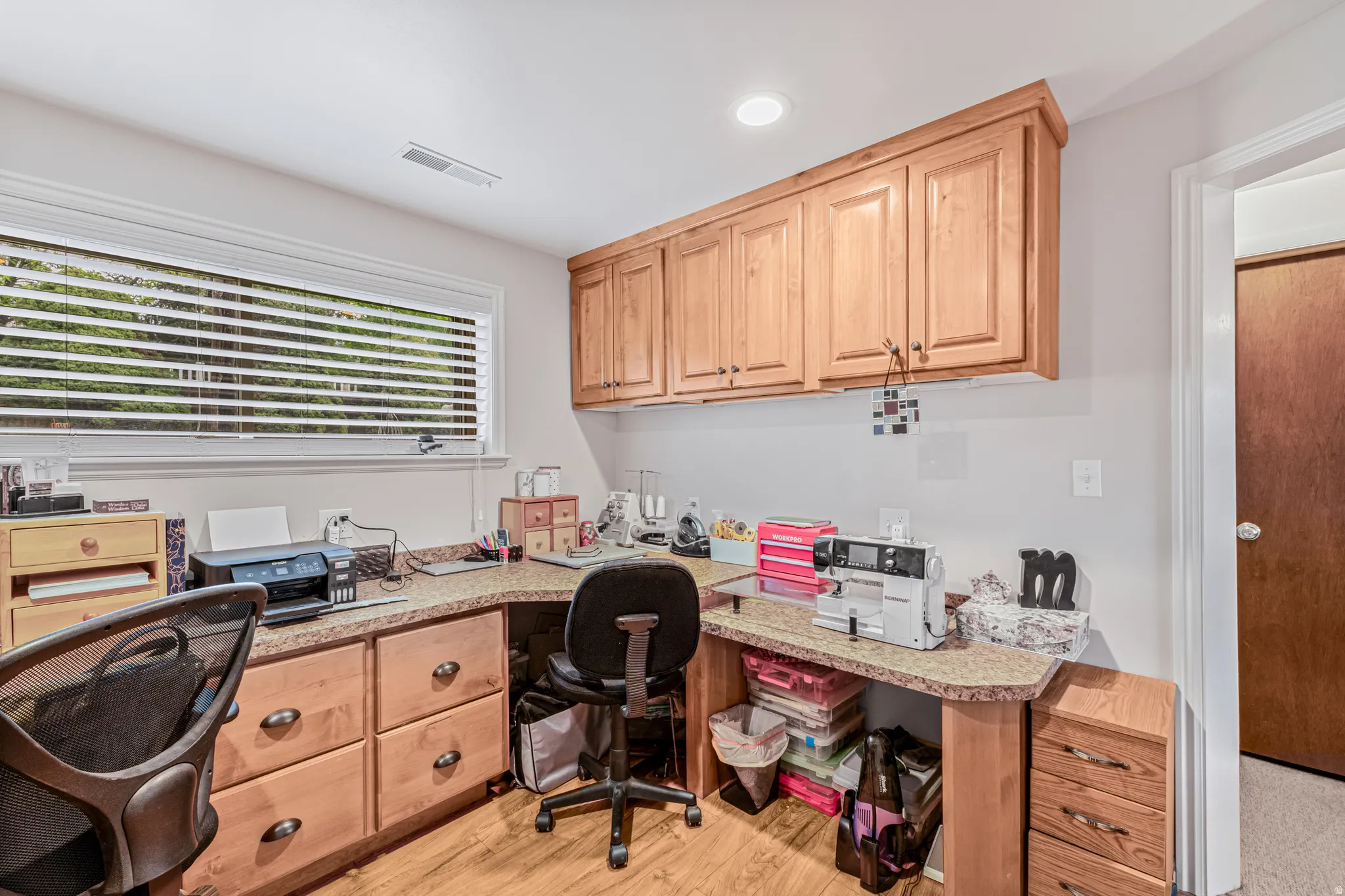 Built-in wood-finish cabinetry, a wrap-around laminate countertop, wood-finish flooring, and a window with horizontal blinds