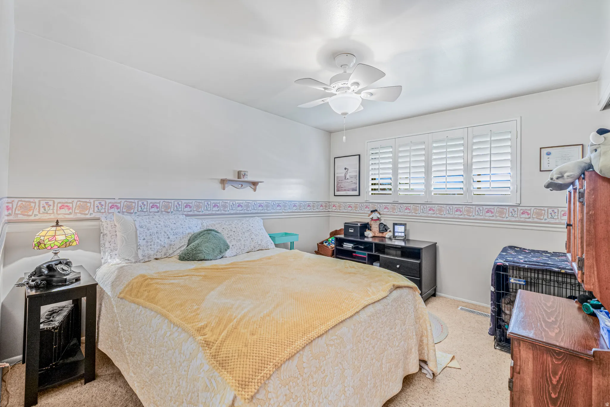 Bedroom featuring a ceiling fan, window with white plantation shutters, and light-toned walls