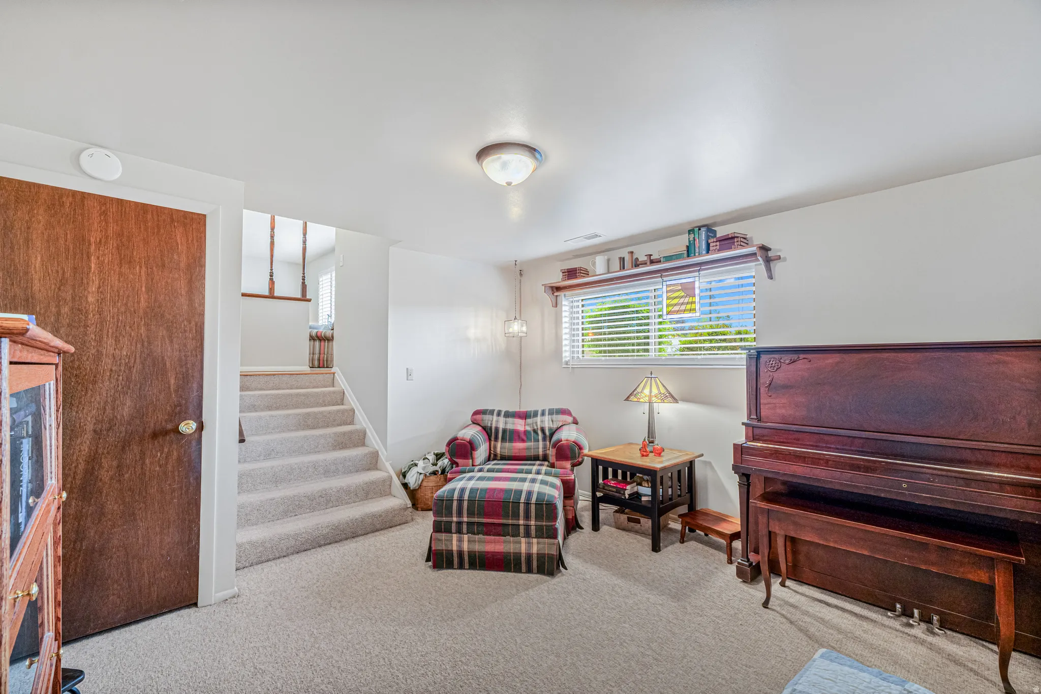 Carpeted stairs with wood balusters, a dark wood-finish door, and a horizontal window with blinds