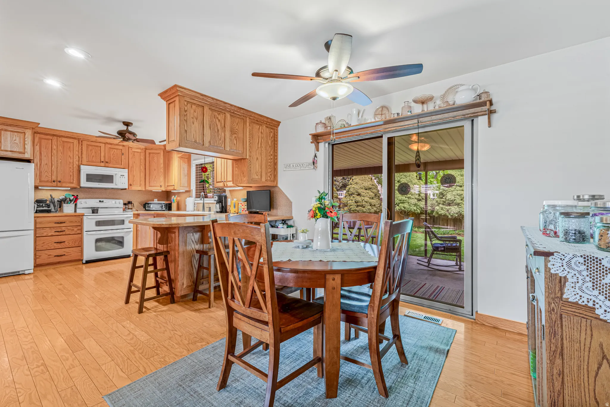 Open-concept kitchen and dining area featuring wood-finish flooring, light wood cabinetry, white appliances, and a kitchen island with seating