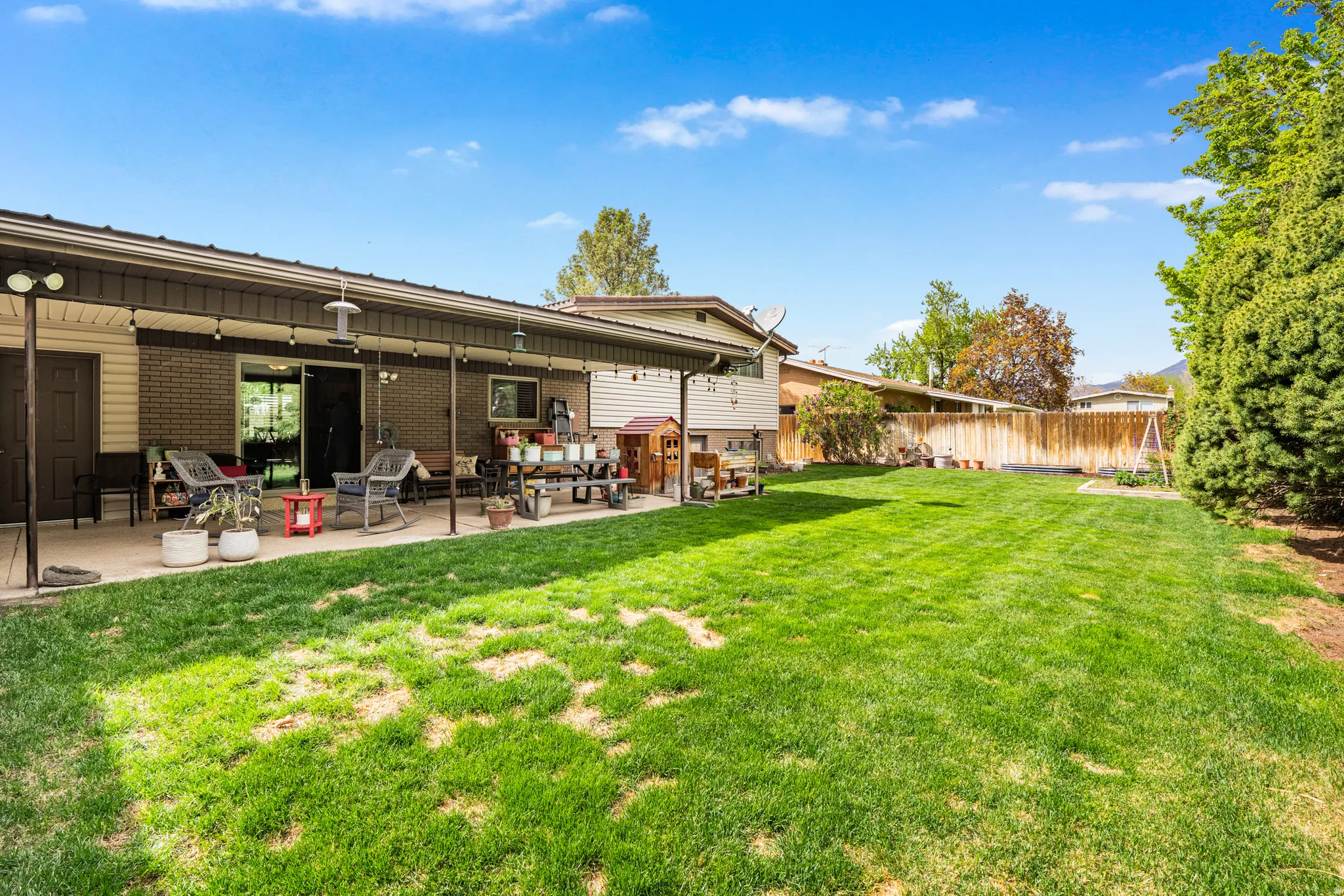 Expansive green lawn with a covered patio, brick exterior, and mature perimeter trees