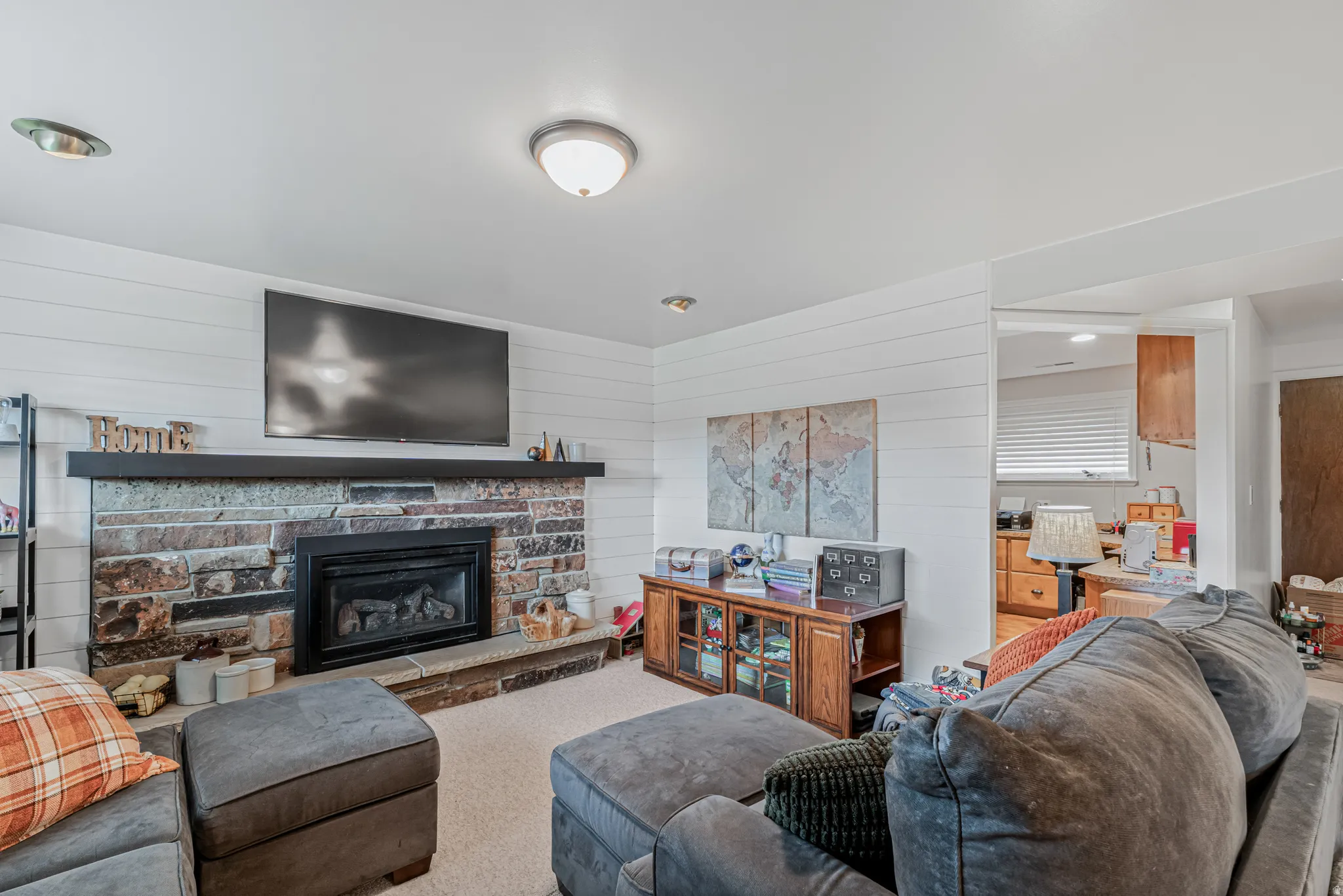 Living area featuring a stone-clad fireplace with a dark wood mantel, shiplap accent wall, and recessed lighting