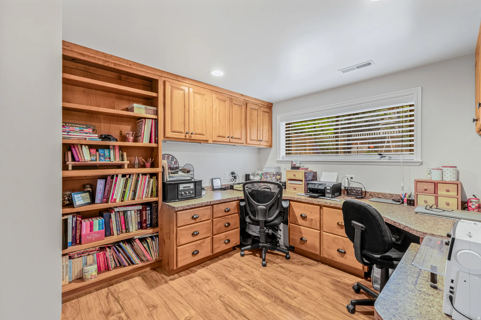 Dedicated workspace featuring custom wood cabinetry, extensive built-in shelving, durable wood-finish flooring, and recessed ceiling lighting