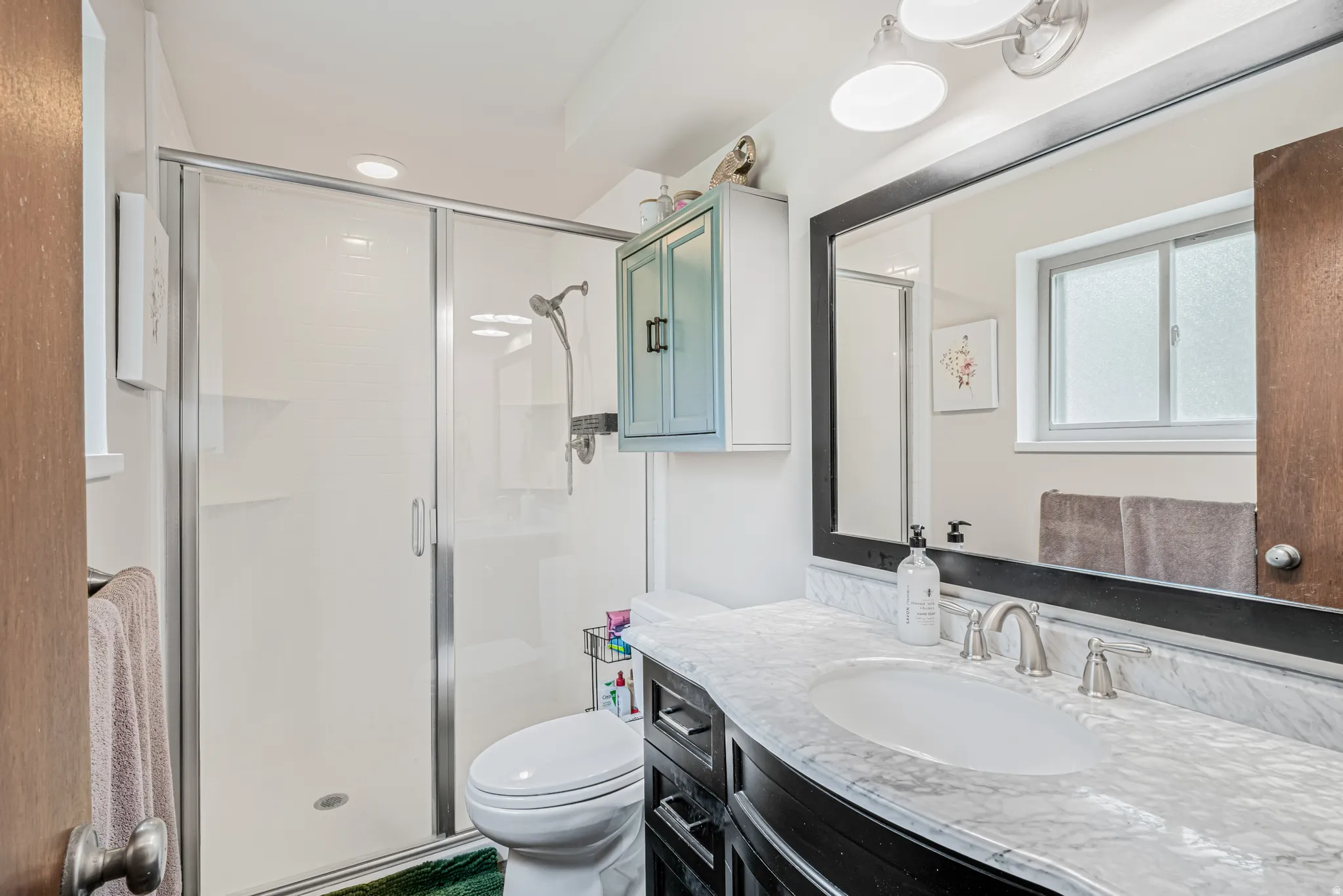 Bathroom featuring a glass-enclosed shower, a vanity with a white stone countertop, a framed mirror, and a window with frosted glass