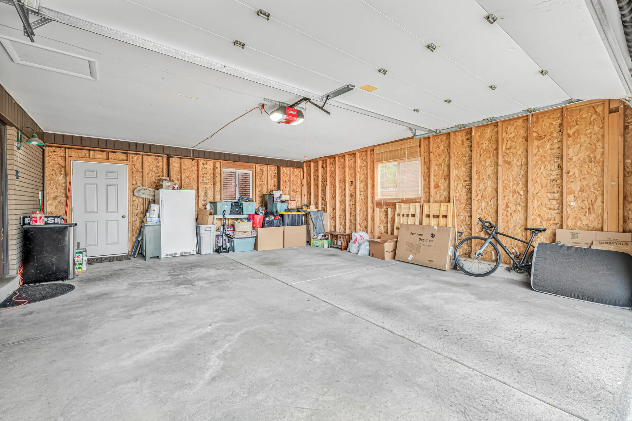 Spacious garage featuring concrete flooring, an overhead door with an automatic opener, exposed wood framing, and two windows providing natural light