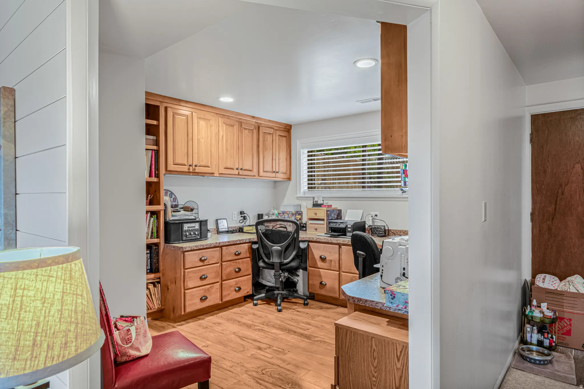 Dedicated workspace featuring wood-finish flooring, extensive built-in cabinetry, integrated shelving, a large window, and recessed lighting