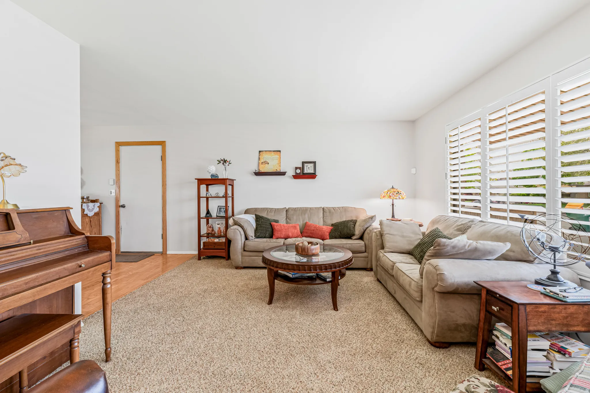 Bright living area featuring textured carpet flooring, white interior walls, and multiple windows with white plantation shutters