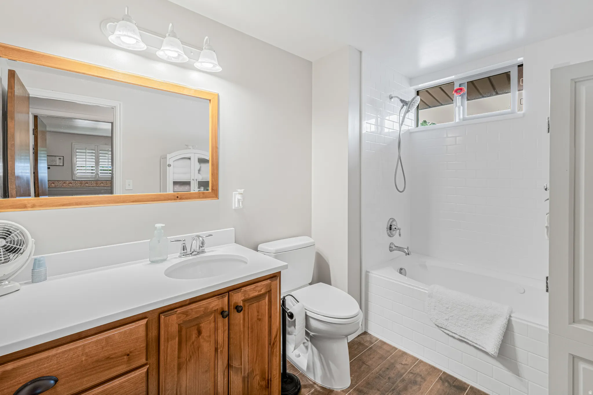Bathroom featuring a wood-finish vanity with a white countertop and integrated sink, a large wood-framed mirror, and a full bathtub with white subway tile surround and an overhead window