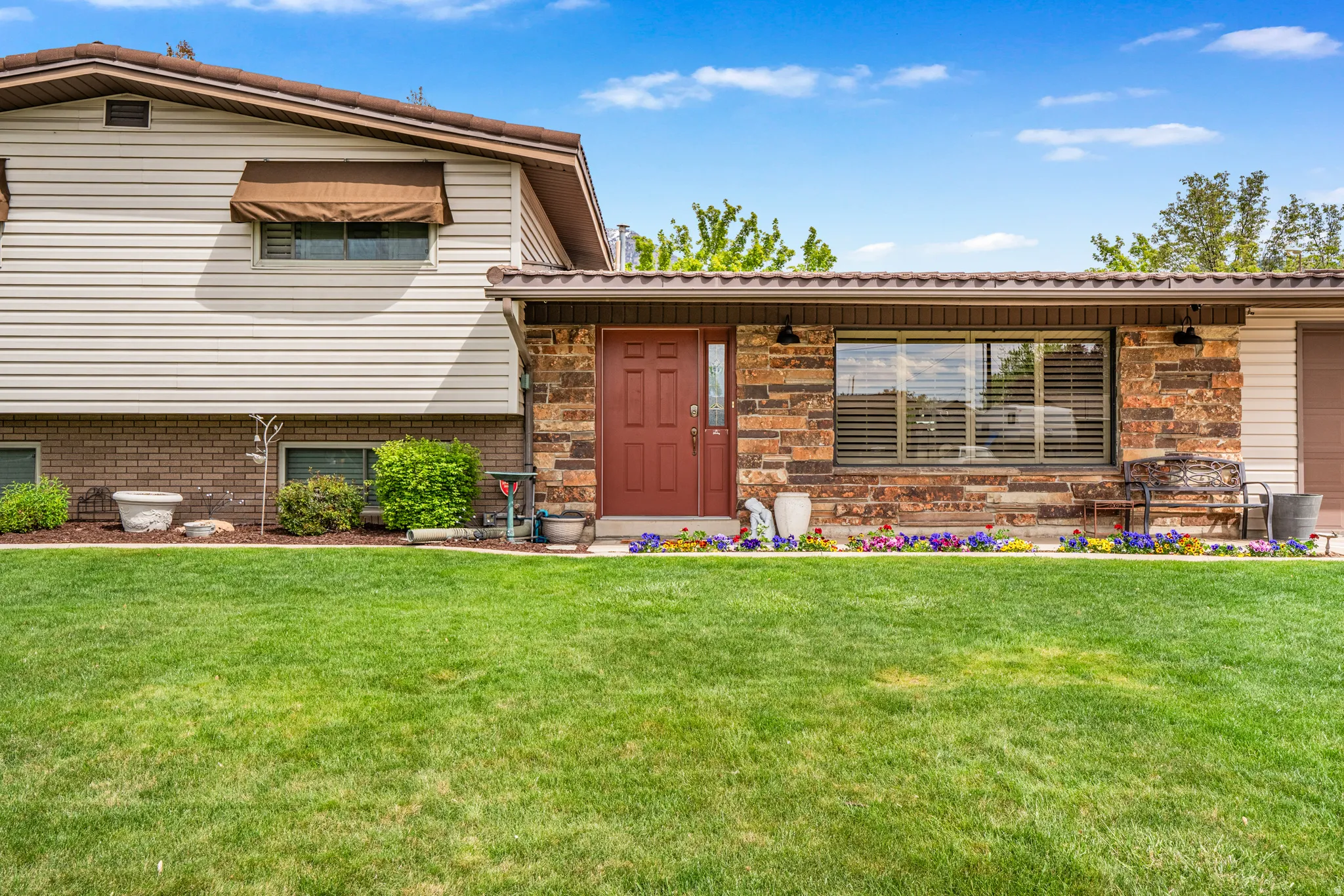 Exterior featuring a red entry door, stone and siding facade, and a neatly manicured lawn