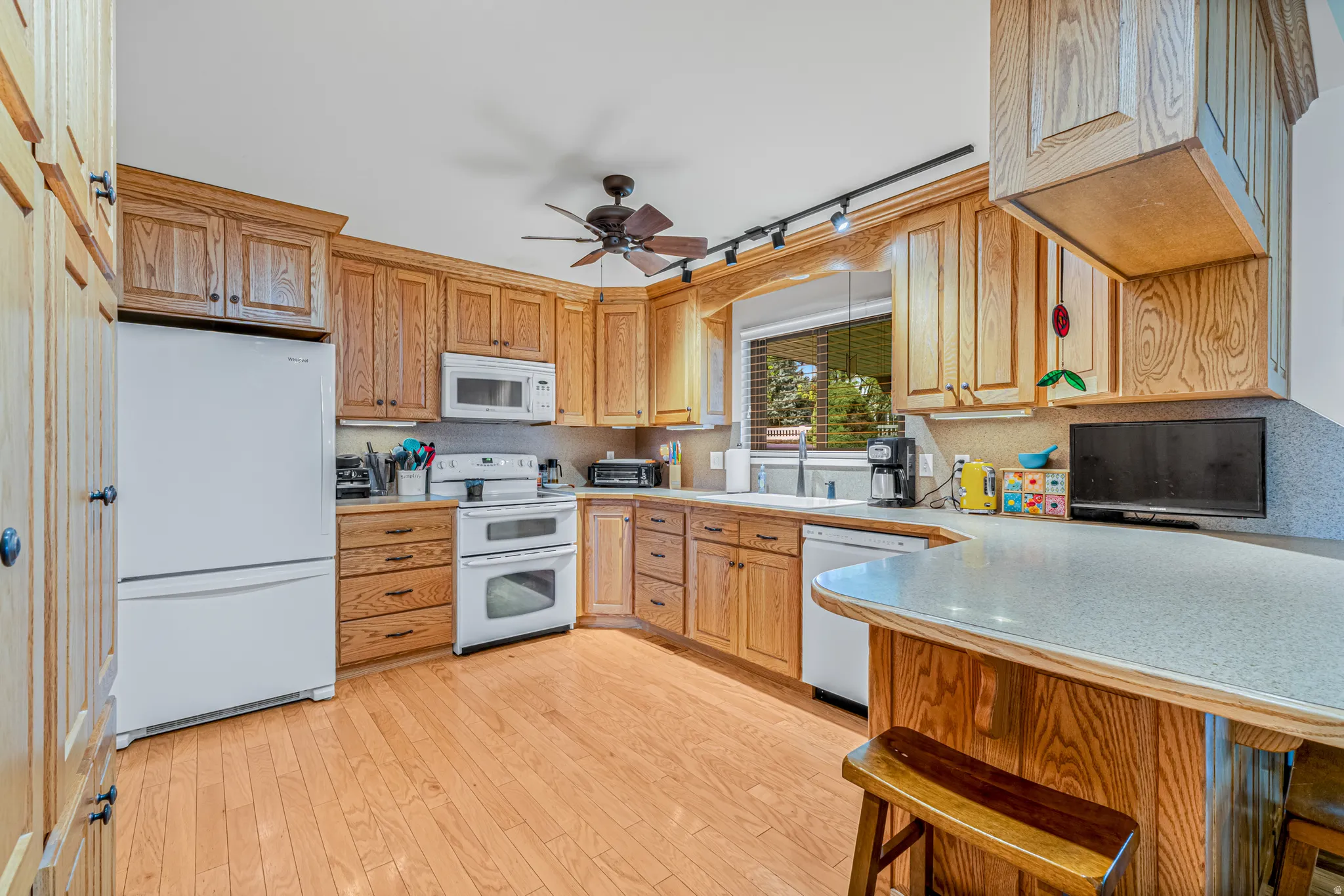 Kitchen featuring wood-finish flooring, wood cabinetry with paneled doors, white appliances, a double oven, and a peninsula with a raised countertop