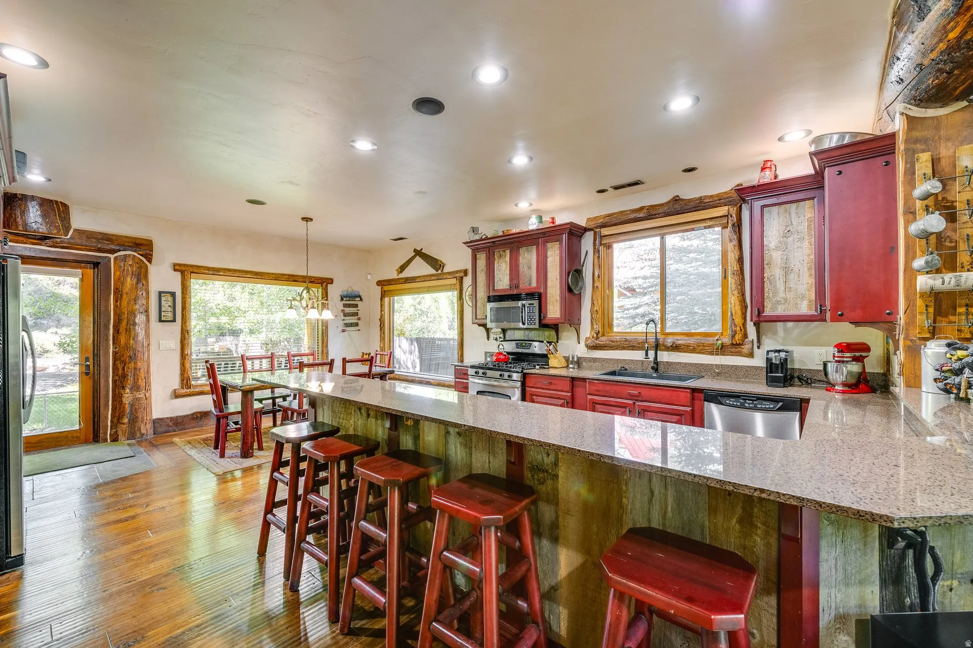 Open-concept kitchen featuring a spacious counter-height peninsula with seating, rich wood-finish flooring, recessed lighting, red cabinetry, and stainless steel appliances