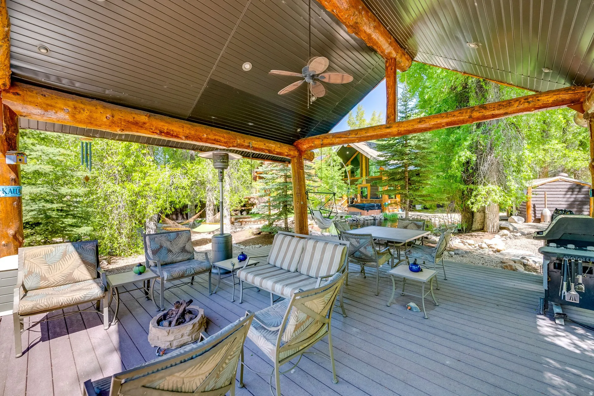 Expansive covered deck featuring a corrugated metal ceiling with exposed log beams and a built-in ceiling fan