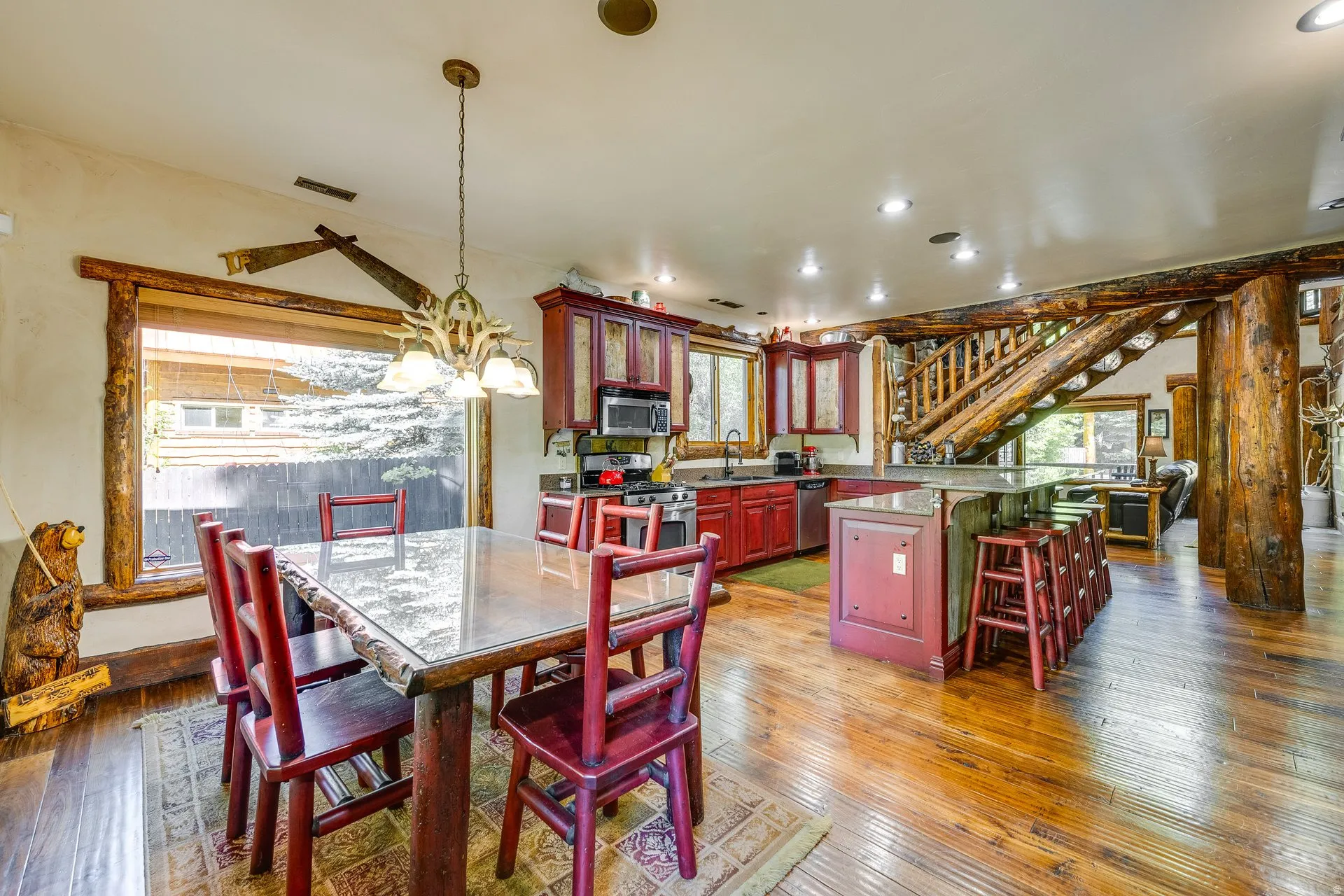 Open-concept kitchen and dining area featuring rich wood-finish flooring, a full suite of stainless steel appliances, a kitchen island with counter seating, and log-style architectural elements