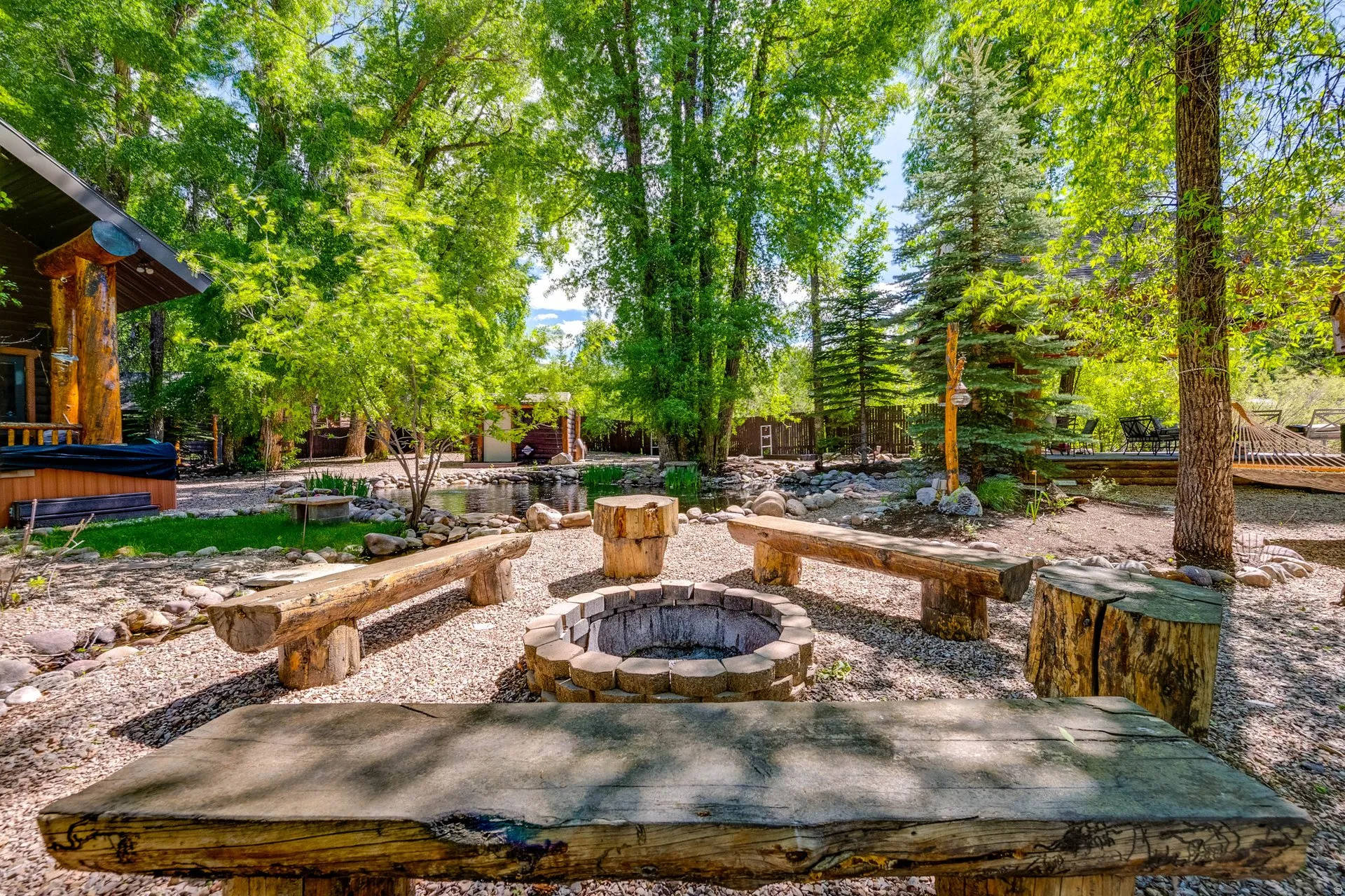Outdoor entertainment area featuring a stone fire pit with surrounding log benches and stump seating
