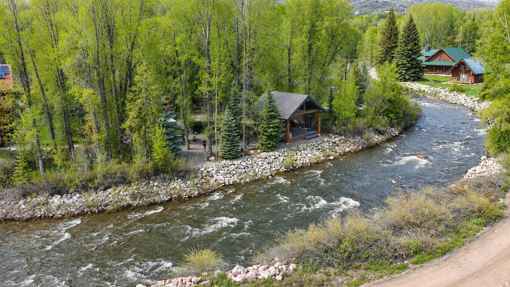Riverfront property featuring a covered outdoor structure, mature trees, and natural rock accents