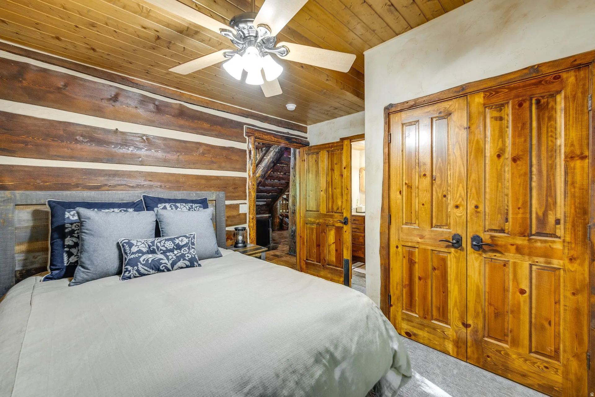 Wood-paneled ceiling with a ceiling fan, log walls, wood-paneled doors, and carpeted flooring