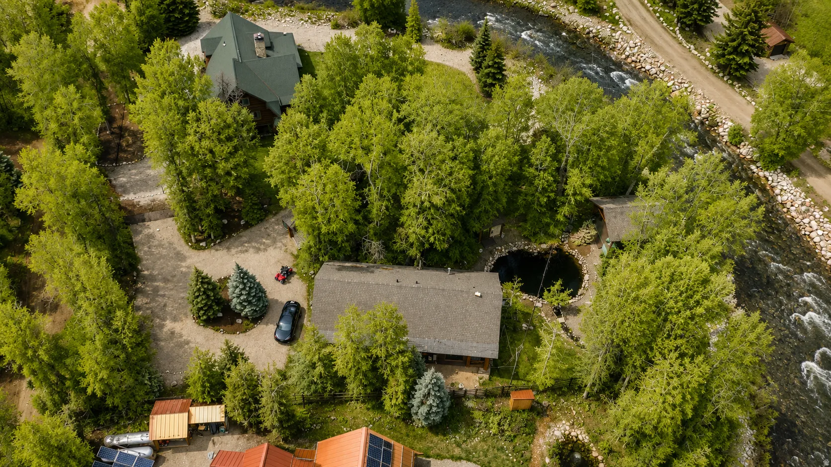 Riverside property featuring a main residence, an additional dwelling, mature trees, and a circular water feature