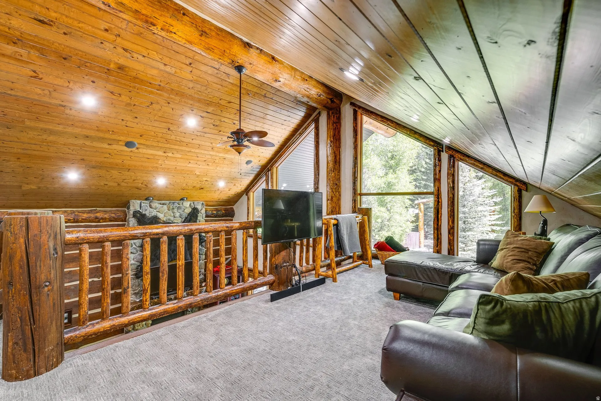 Loft area featuring sloped wood-paneled ceilings, exposed wood beams, and large picture windows