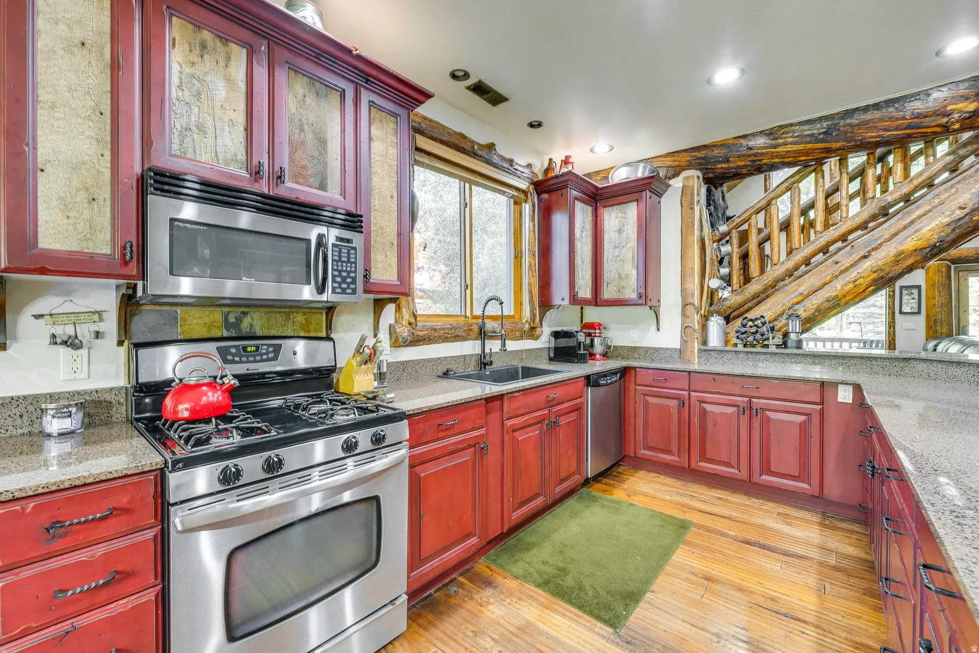 Kitchen featuring rustic red cabinetry with glass-front uppers, wood-finish flooring, and a stainless steel appliance suite including a range and microwave