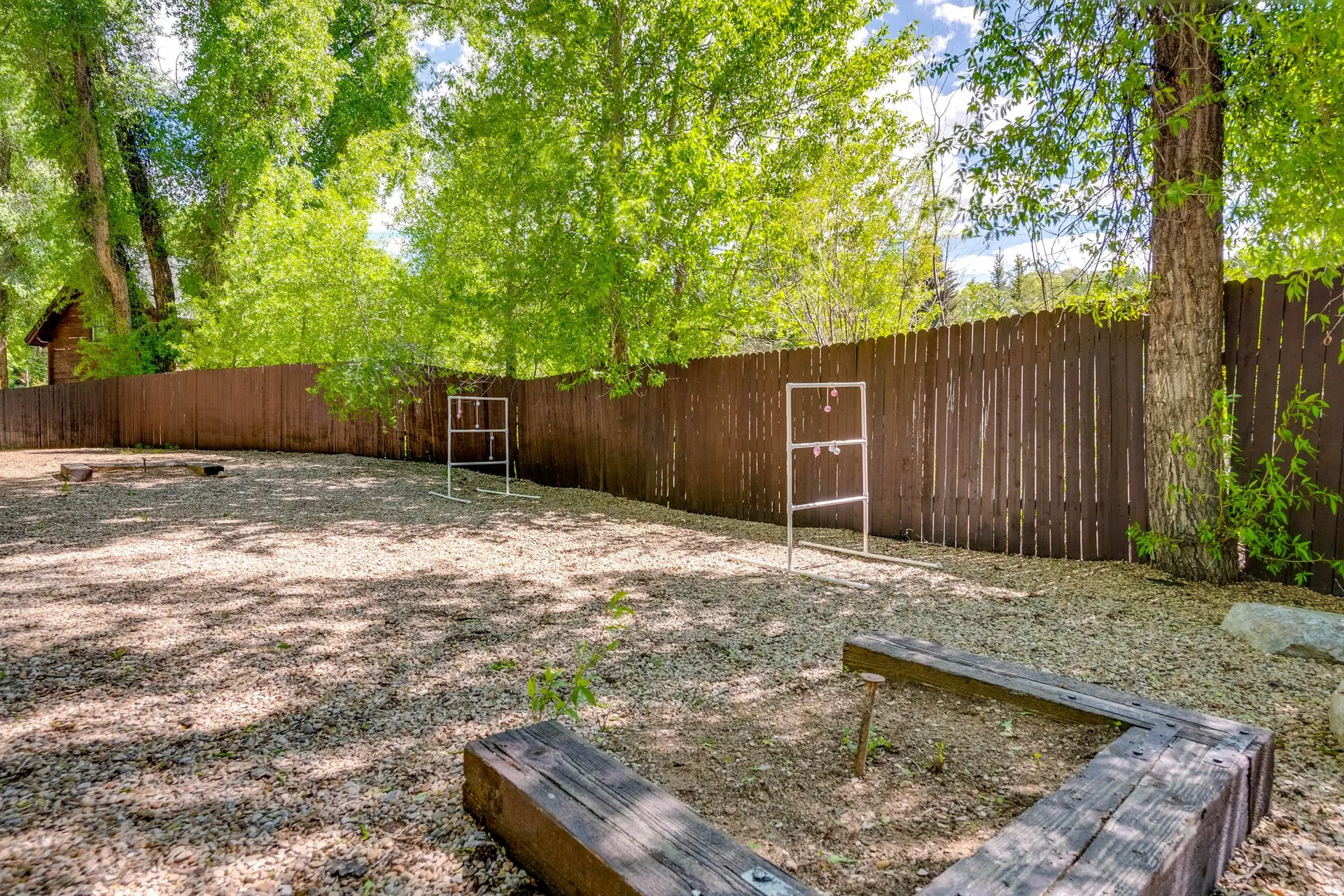 Spacious outdoor area featuring a gravel surface, wood privacy fencing, and mature trees providing natural shade